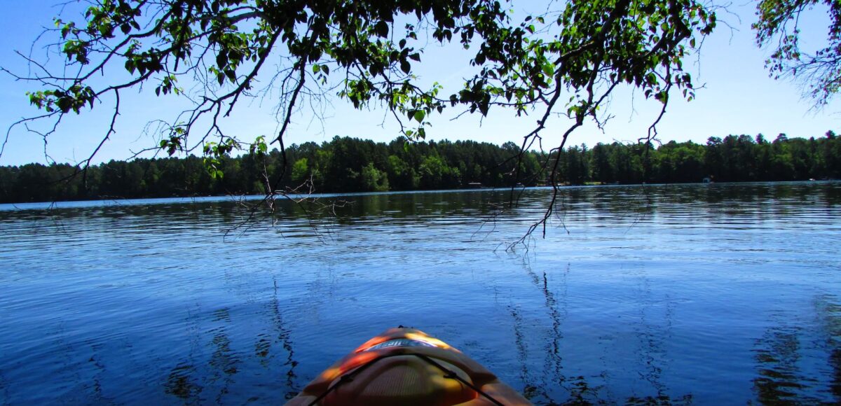 front of kayak on the water framed by trees